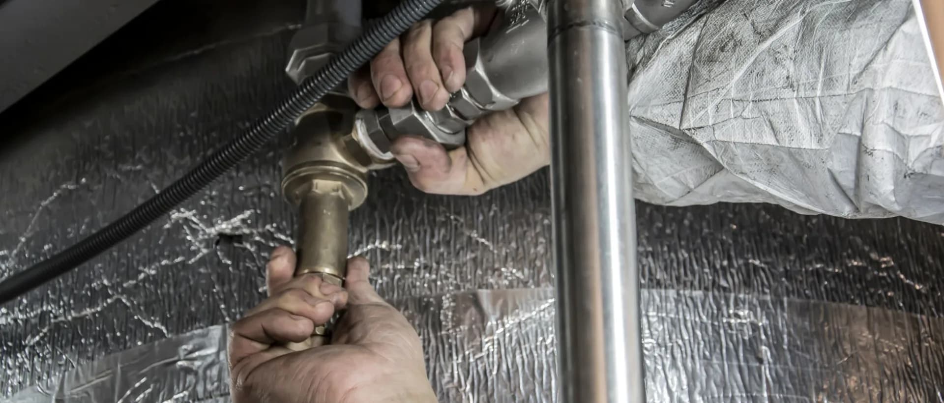 Licensed plumber inspecting a kitchen sink pipe