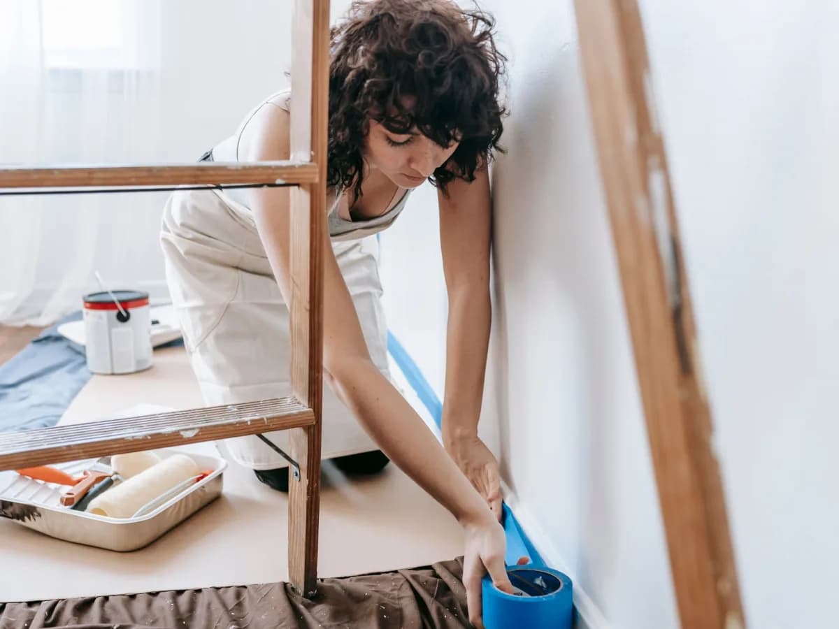 A person examining a wall and using painter's tape to check for problems.