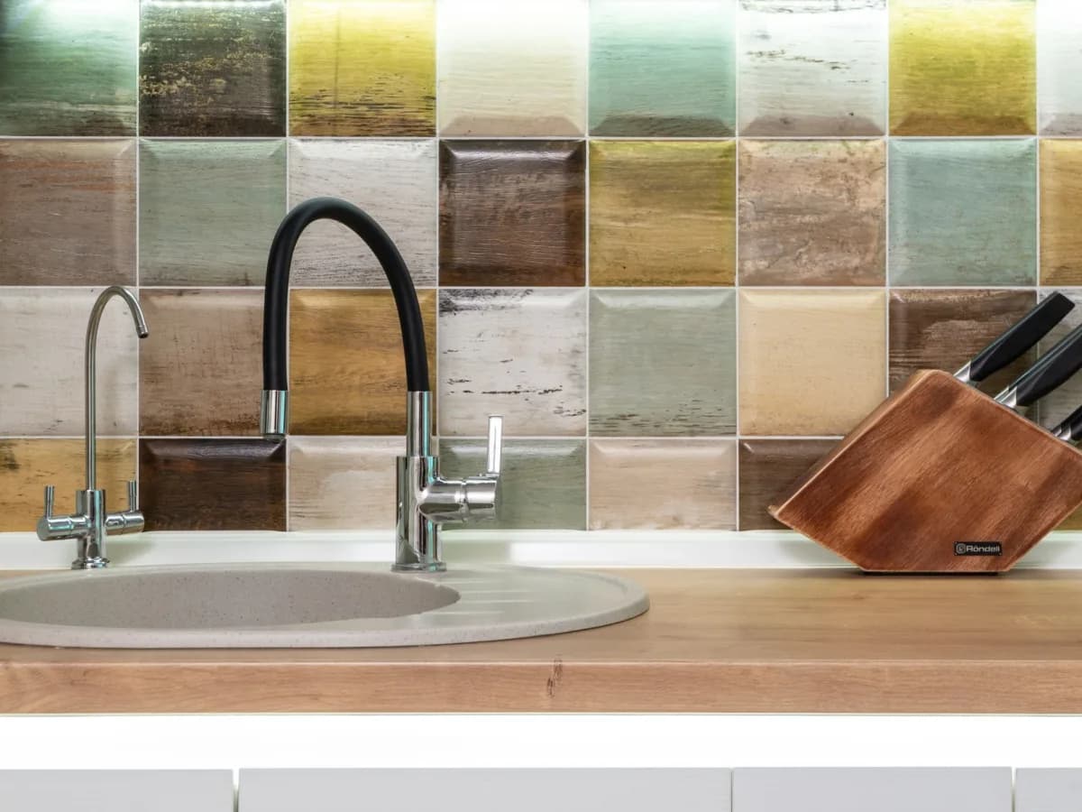 Cracked backsplash tiles and worn grout near a kitchen sink.