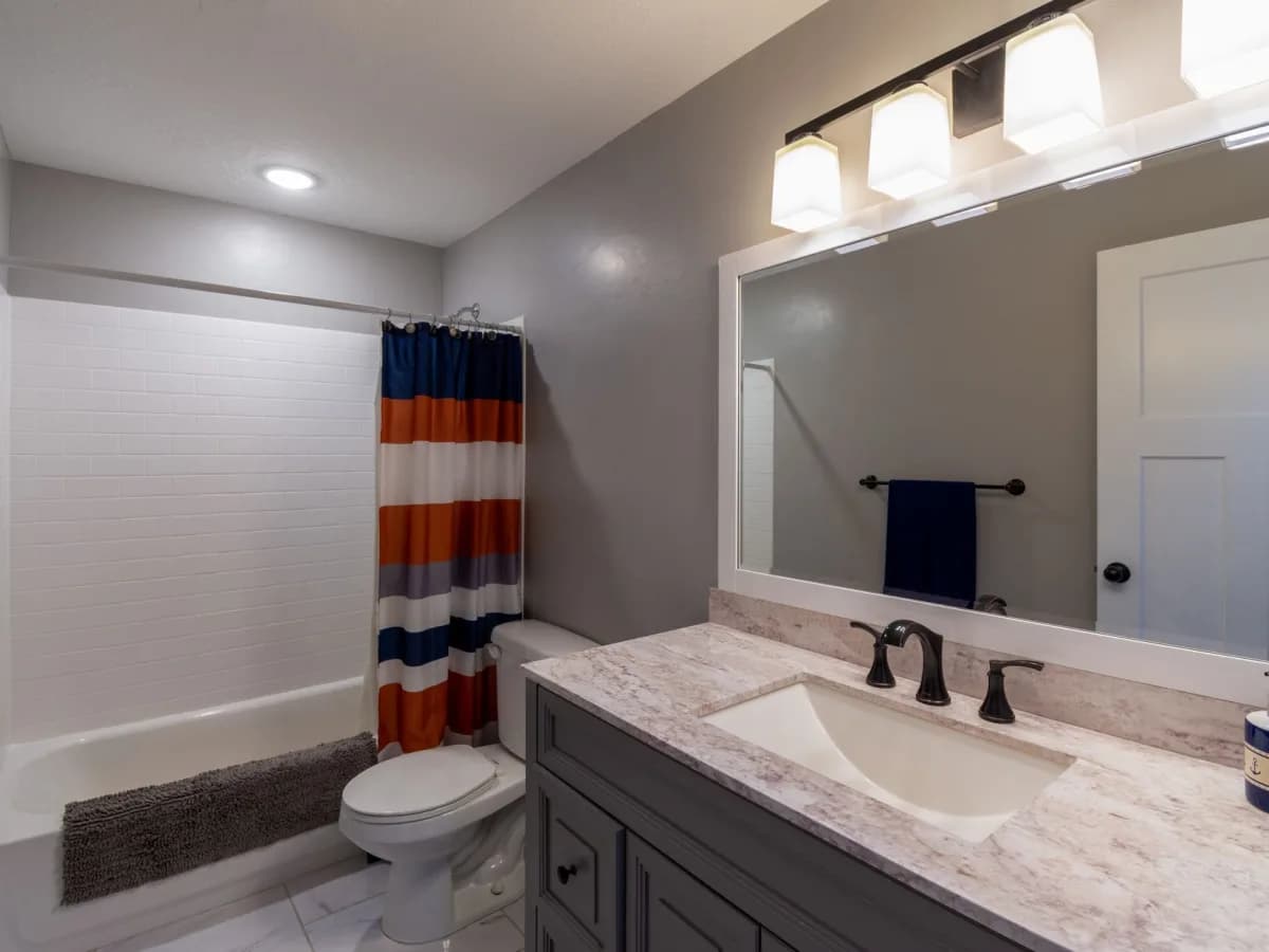 Finished residential bathroom with vanity, toilet, tiled floor, and tiled tub surround.